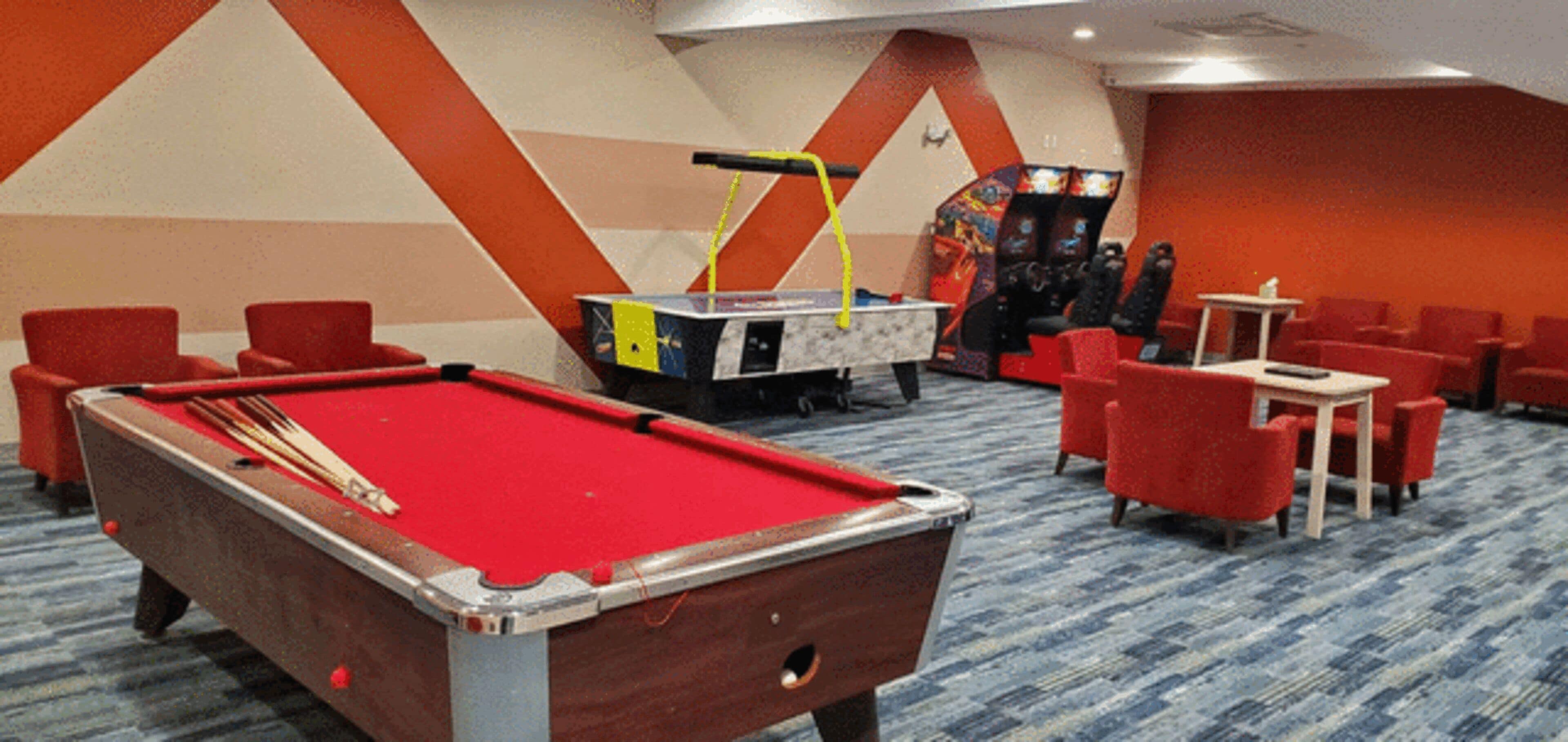 A pool table with a red felt surface, surrounded by red chairs and a small table with a remote control.