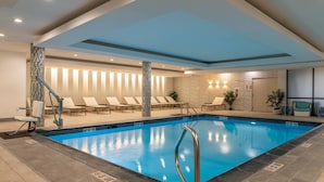 A swimming pool with lounge chairs, a staircase, and a wall with vertical light panels.
