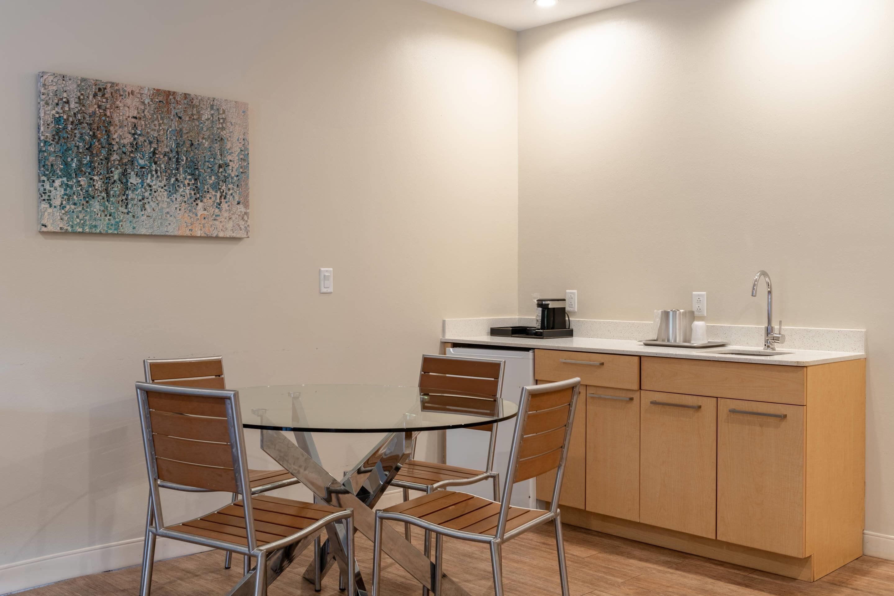 Una cocina moderna con una mesa de comedor de vidrio, sillas de madera y una cafetera.