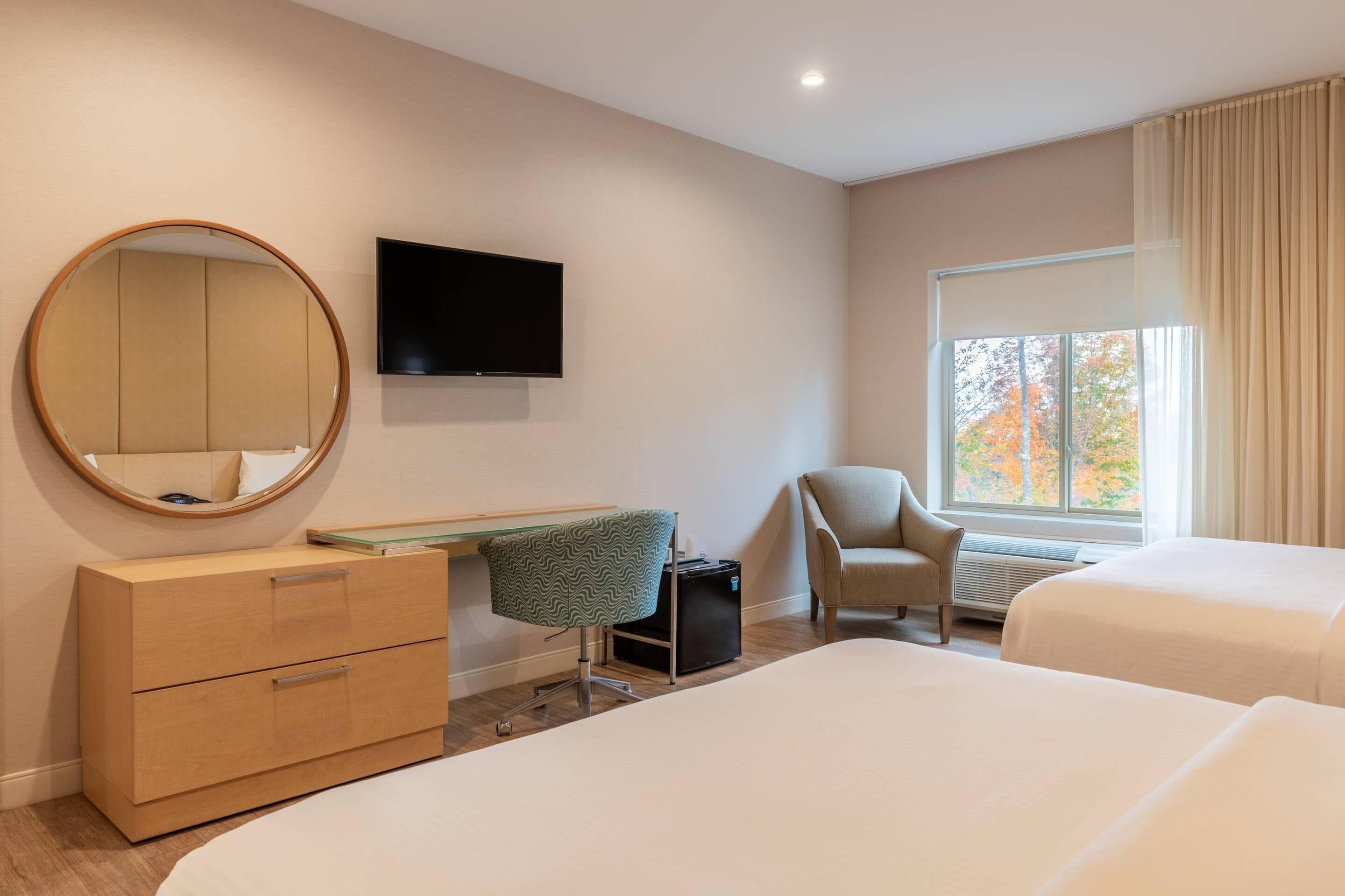 Ein Hotelzimmer mit Bett, Sessel, Schreibtisch, Fernseher und einem Fenster mit Vorhängen.