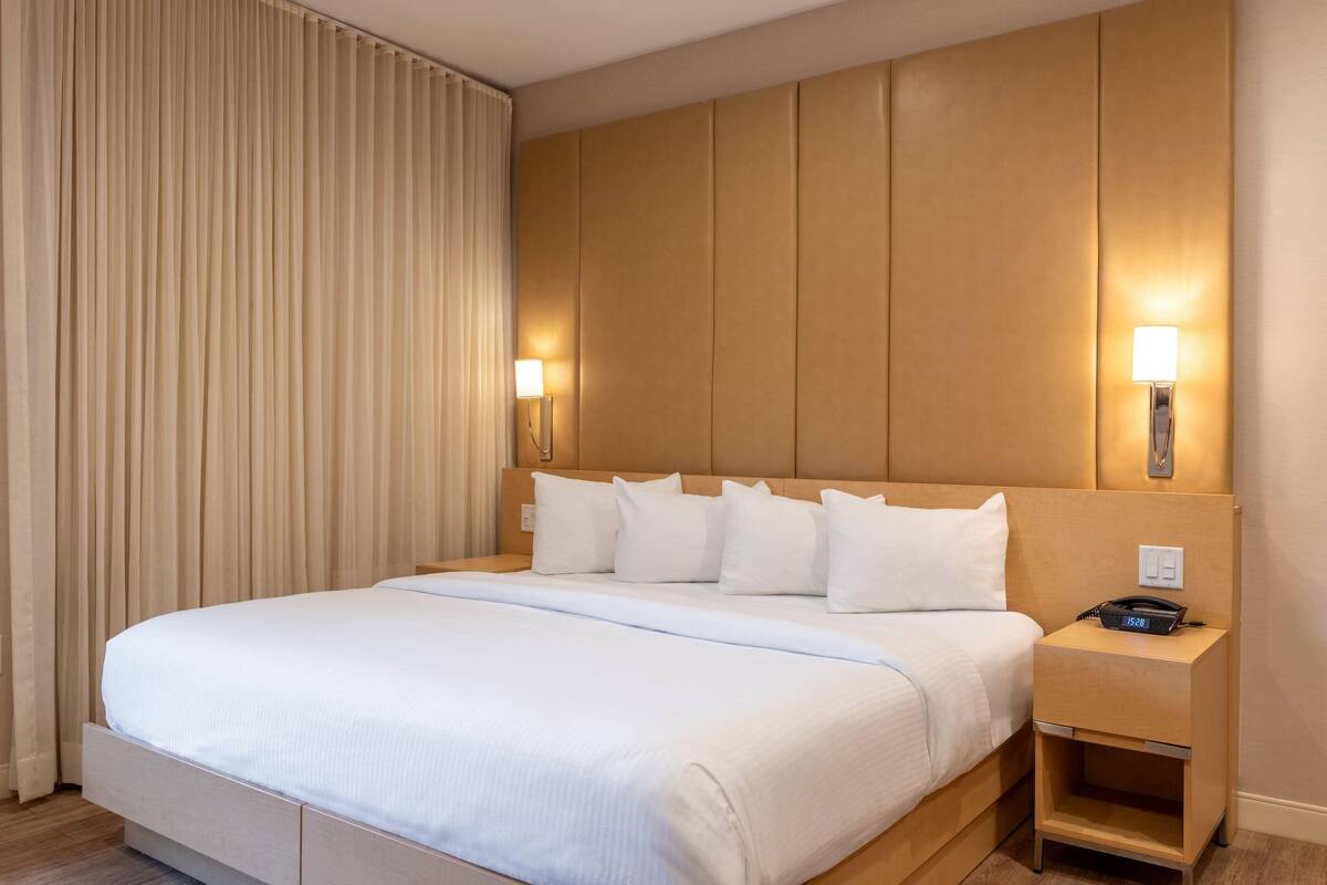 A hotel room with a large bed, a wooden headboard, two bedside tables with lamps, and a curtain on the window.