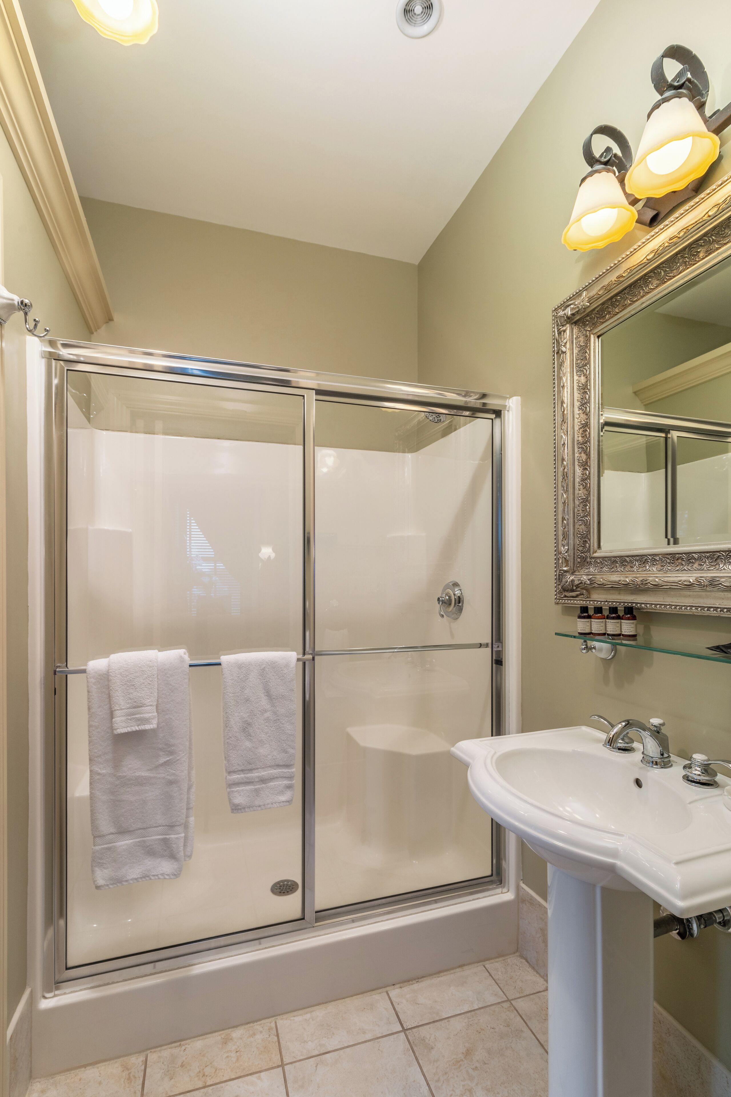 A bathroom with a glass-enclosed shower, a white sink, and a mirror with a decorative frame.