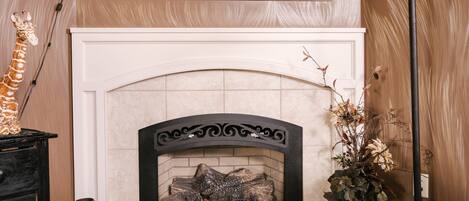 A fireplace with a mantel decorated with various items, a framed picture above, and a vase with dried flowers to the right.