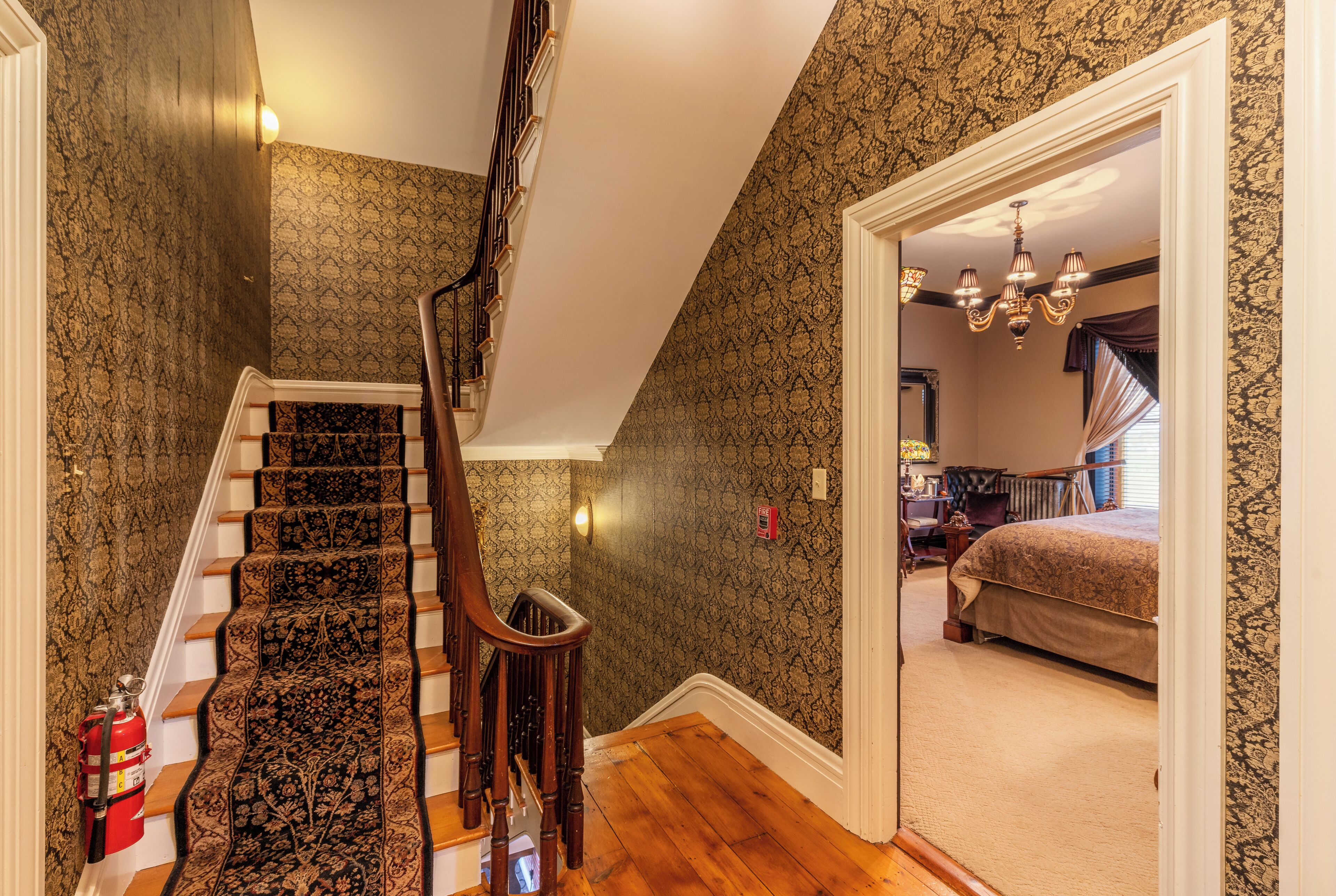 A staircase with a patterned carpet, a wooden handrail, and a fire extinguisher on the wall.
