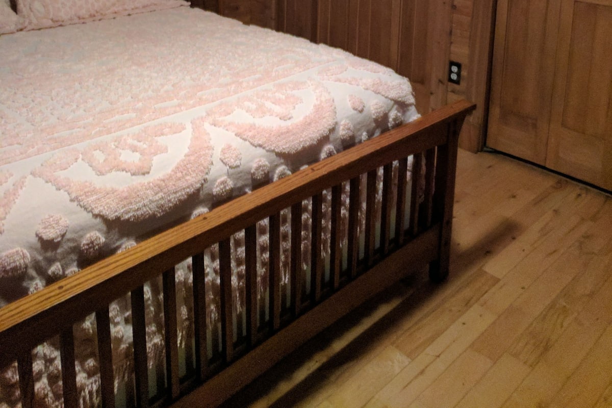 Una habitación de madera con una cama, una mesita de noche y una puerta.