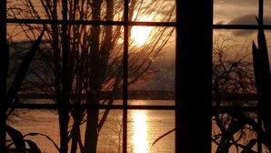 A sunset view through a window with a view of a body of water and trees. - Innisfaire (Traverse City)