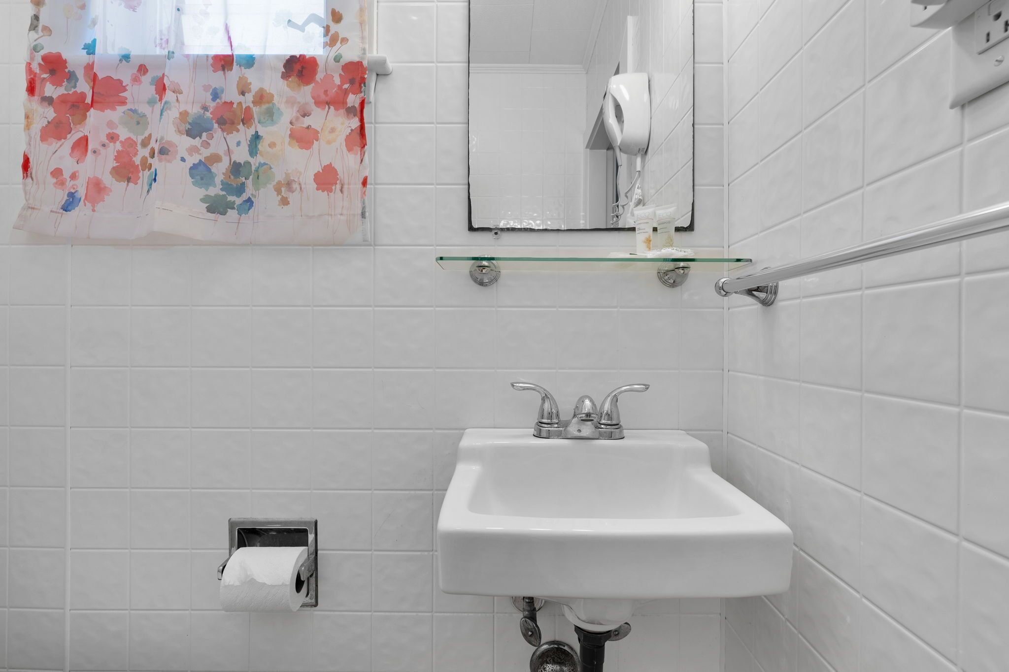 Une salle de bain avec un lavabo blanc, un sèche-mains et un porte-rouleau de papier toilette.