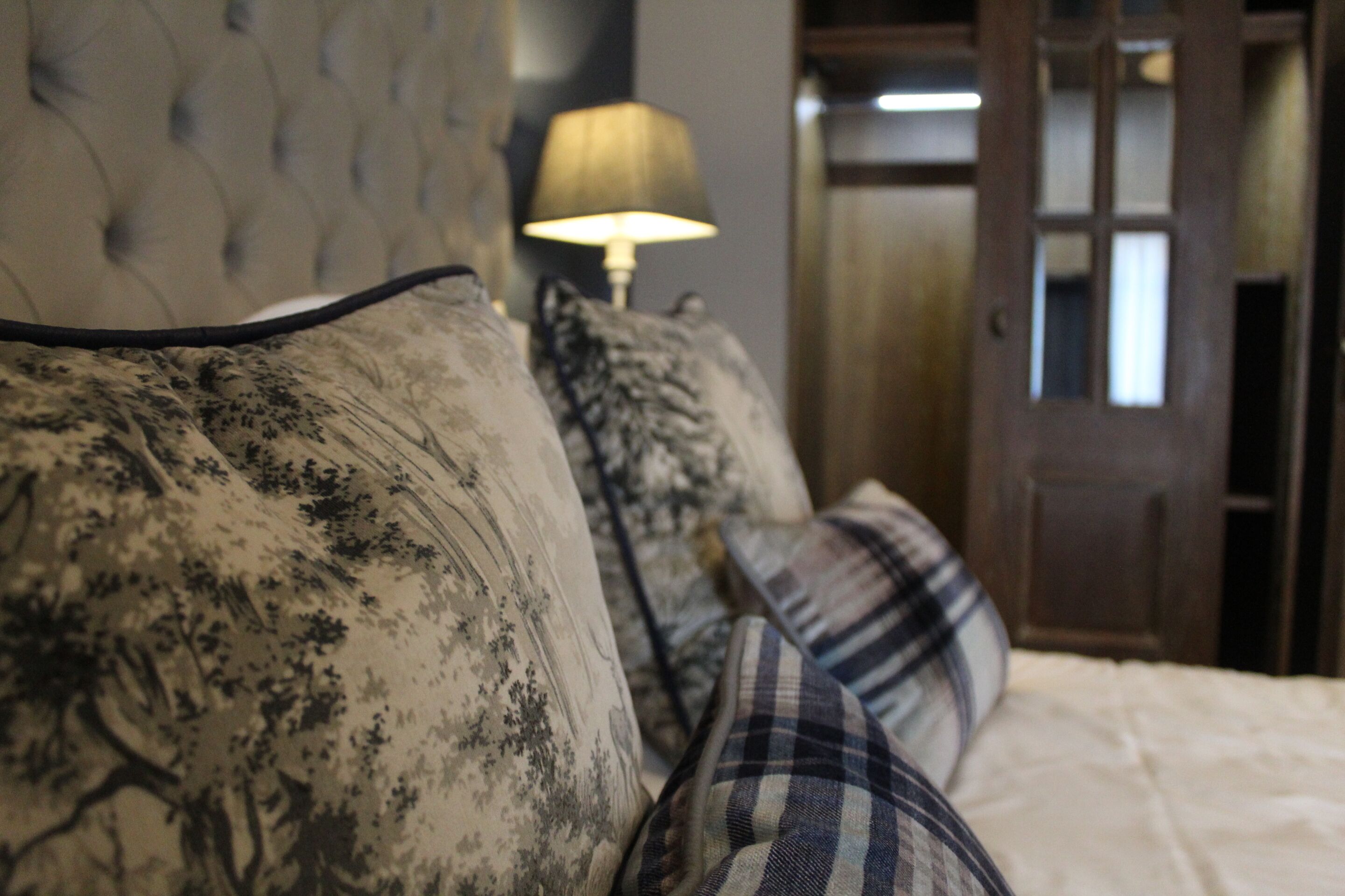 A bedroom with a tufted headboard, a lamp, and a door in the background.