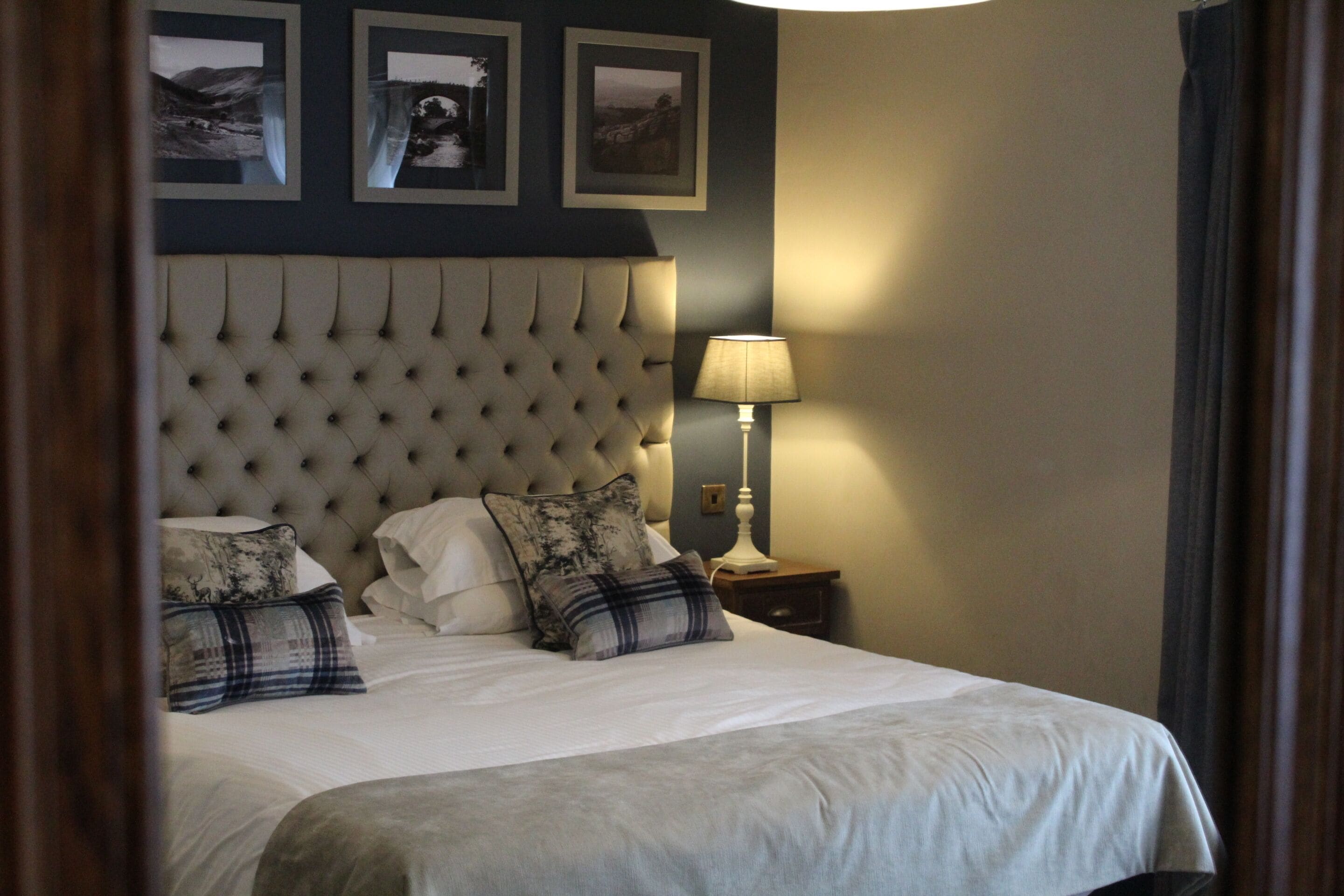A neatly made bed with a tufted headboard, a bedside lamp, and three framed pictures on the wall.