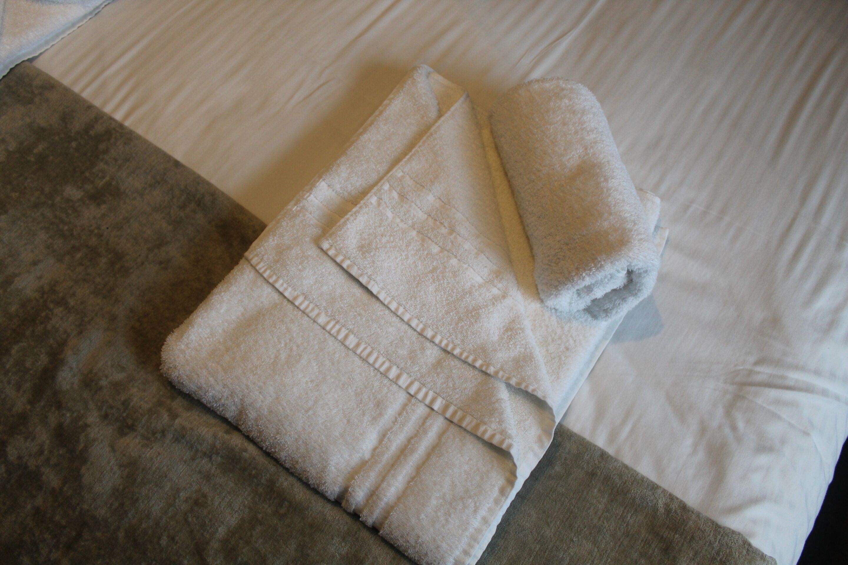 A neatly folded towel on a bed with a grey and white striped pillow.