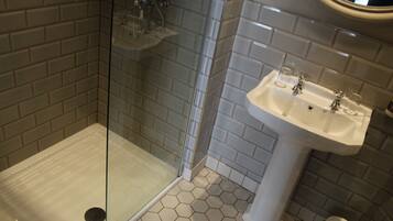 Un baño con ducha acristalada, lavamanos blanco con dos grifos y azulejos de patrón hexagonal.