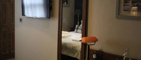 Una camera d'albergo con televisore fissato al muro, una lampada da comodino, un quadro incorniciato e una porta in legno.
