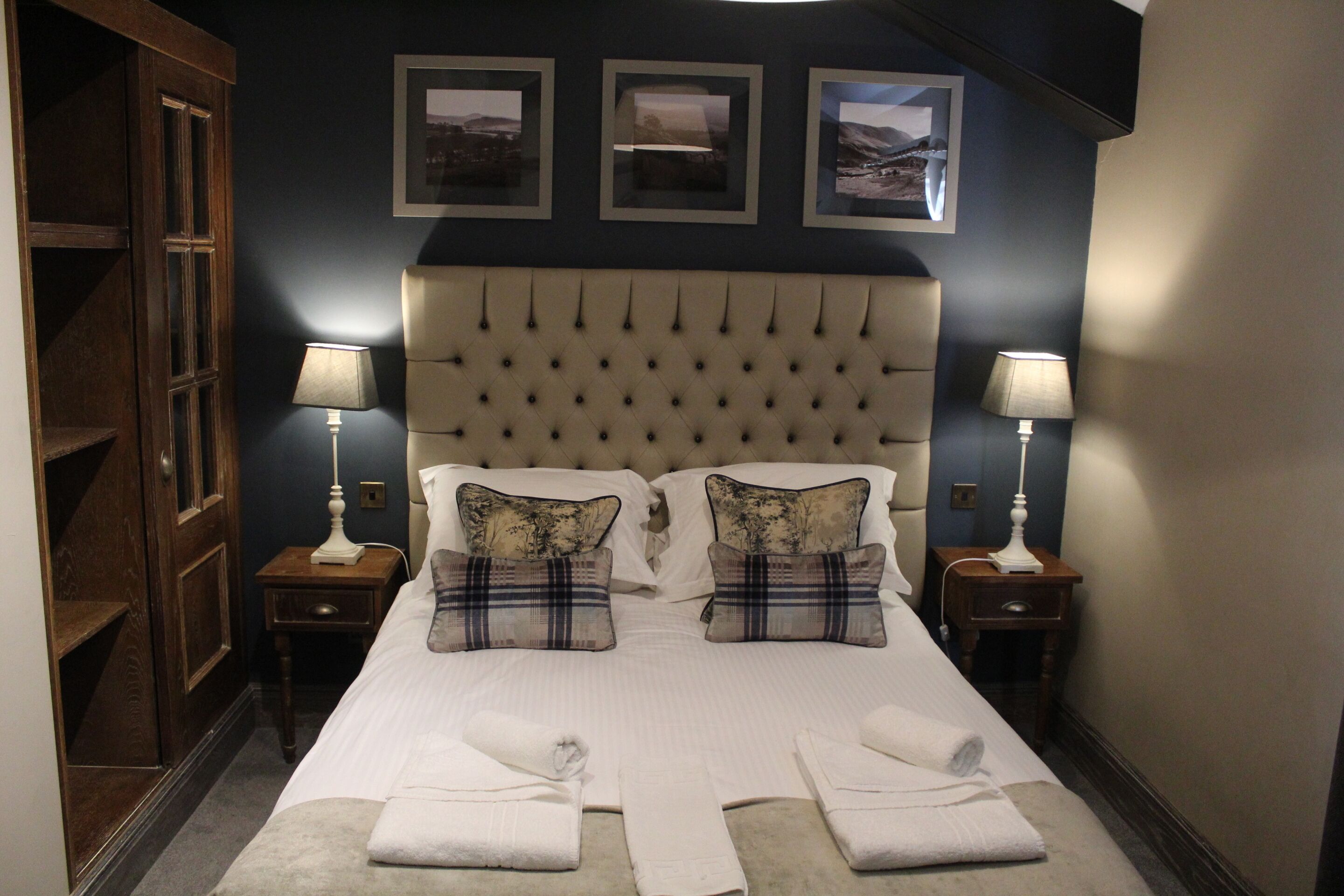 A neatly made bed with two pillows, two bedside tables with lamps, and three framed pictures on the wall.