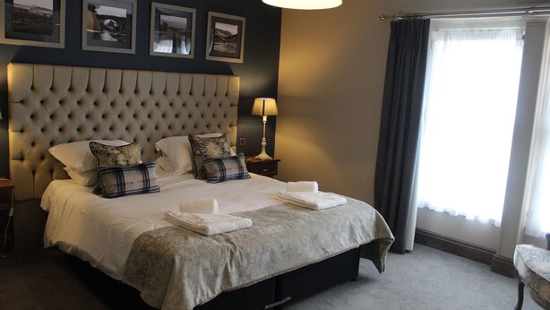 A neatly made bed with a tufted headboard, a bedside lamp, and a view of a window with curtains.