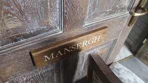A wooden door with a brass handle and a nameplate that reads "MANSERGH".