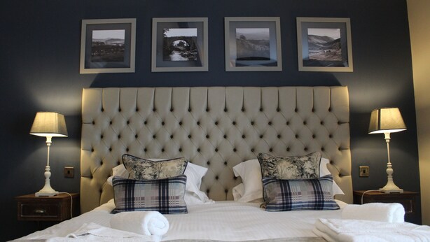 A neatly made bed with a tufted headboard, two bedside tables with lamps, and three framed pictures on the wall. - Red Dragon Inn (Carnforth)