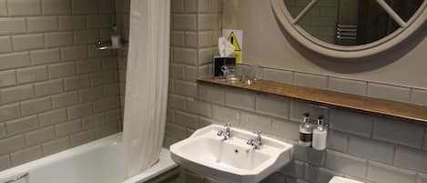 Un baño con bañera, lavamanos y retrete. Hay un estante con artículos de aseo personal y un letrero de precaución.