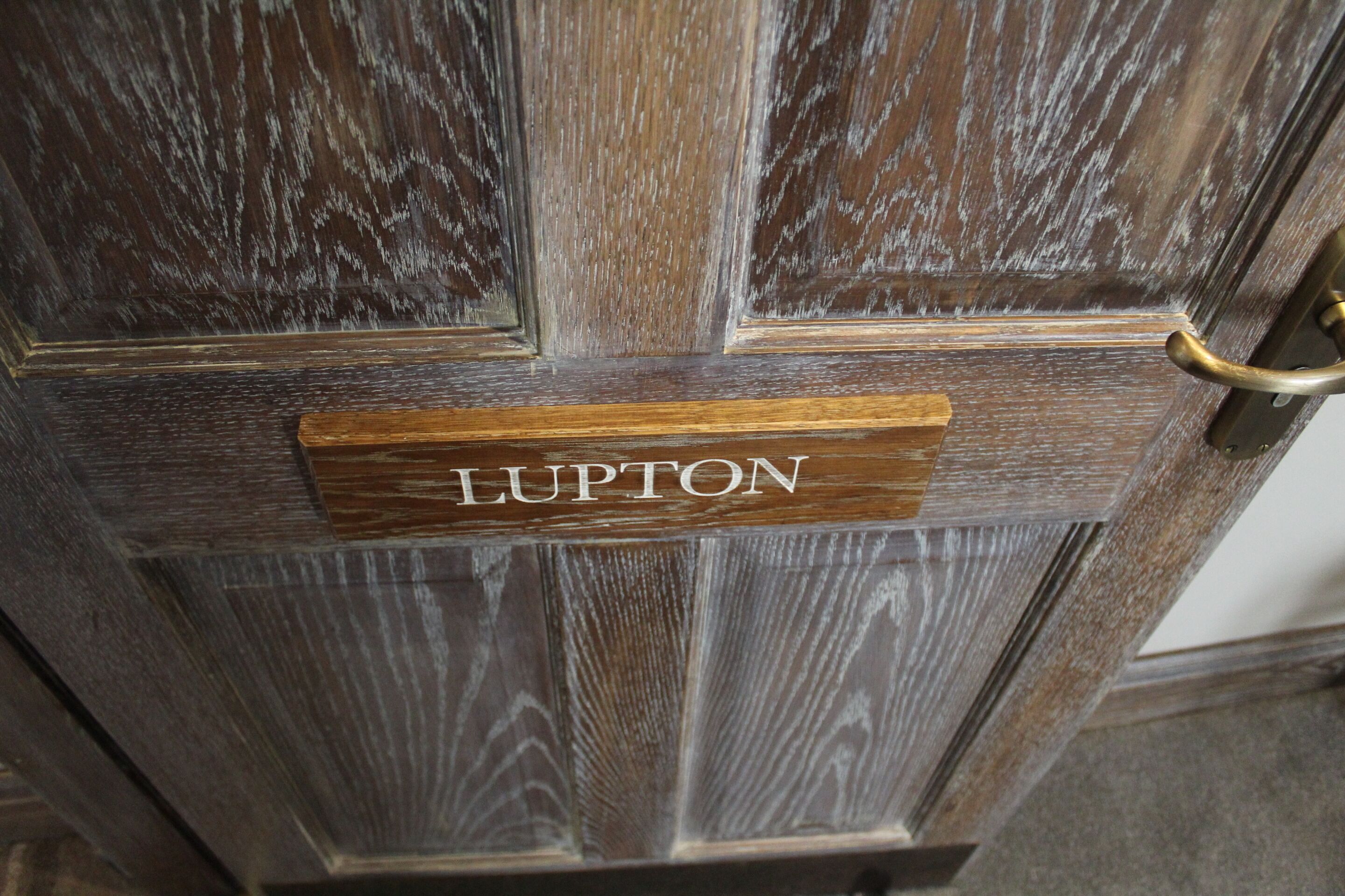 Puinen ovi, jossa on messinkinen vetokahva ja nimikyltti, jossa lukee ”LUPTON”.