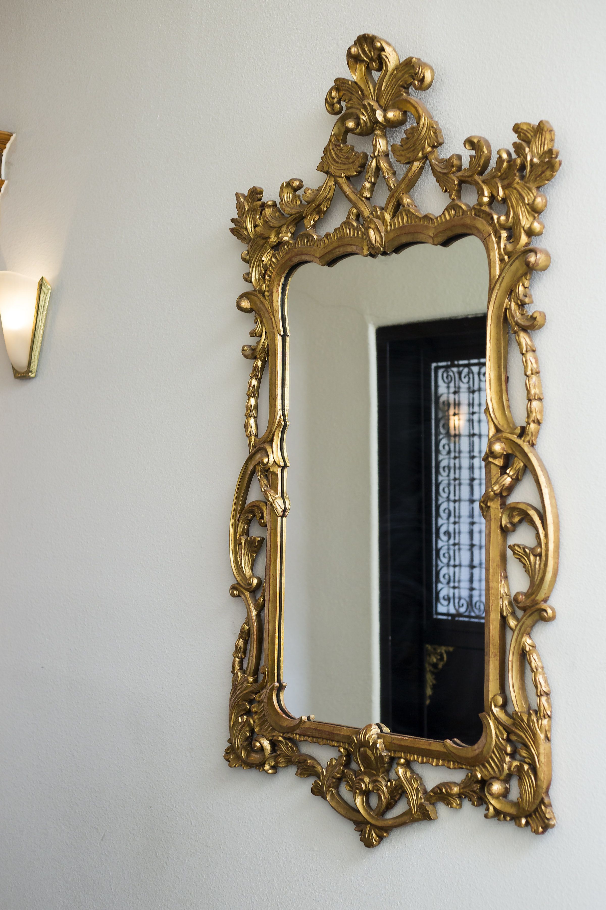 A gold ornate mirror with a decorative frame on a white wall.