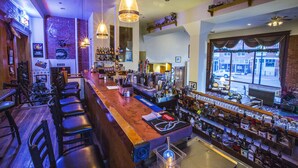 A bar area with a long counter, multiple seating options, and a variety of bottles and glasses on shelves. - Victor Hotel (Victor)