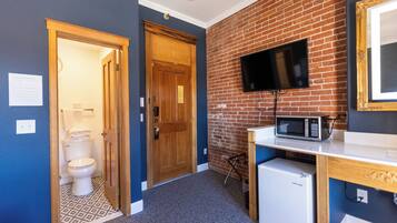 A compact room with a toilet, a wooden door, a brick wall, a television, and a microwave.