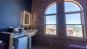 A room with a brick wall, a large arched window, a microwave, and a refrigerator. - Victor Hotel (Victor)