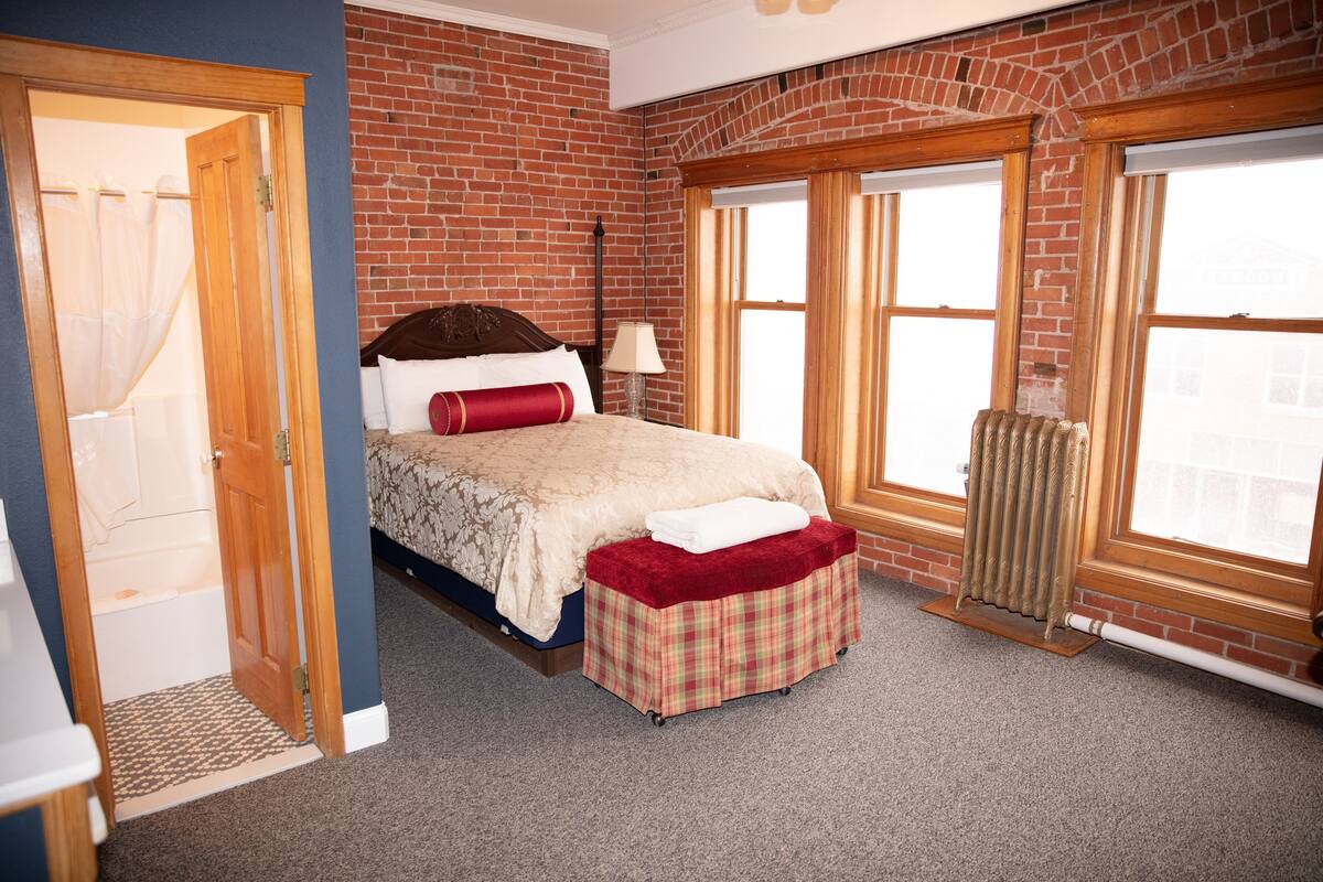 A bedroom with a bed, a radiator, a window, and a door.
