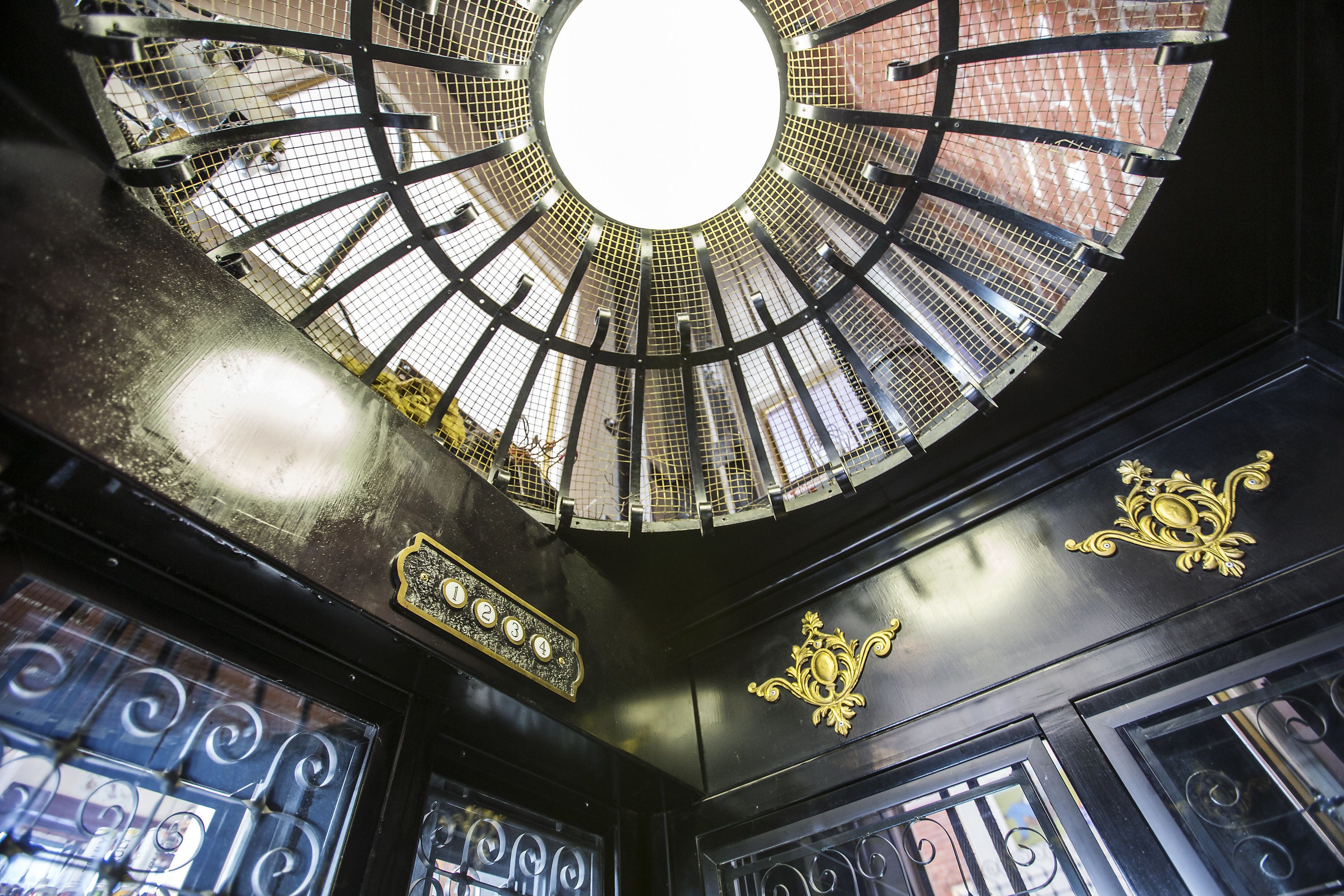 A circular skylight with a metal grid design, ornate gold detailing, and a central white light source.