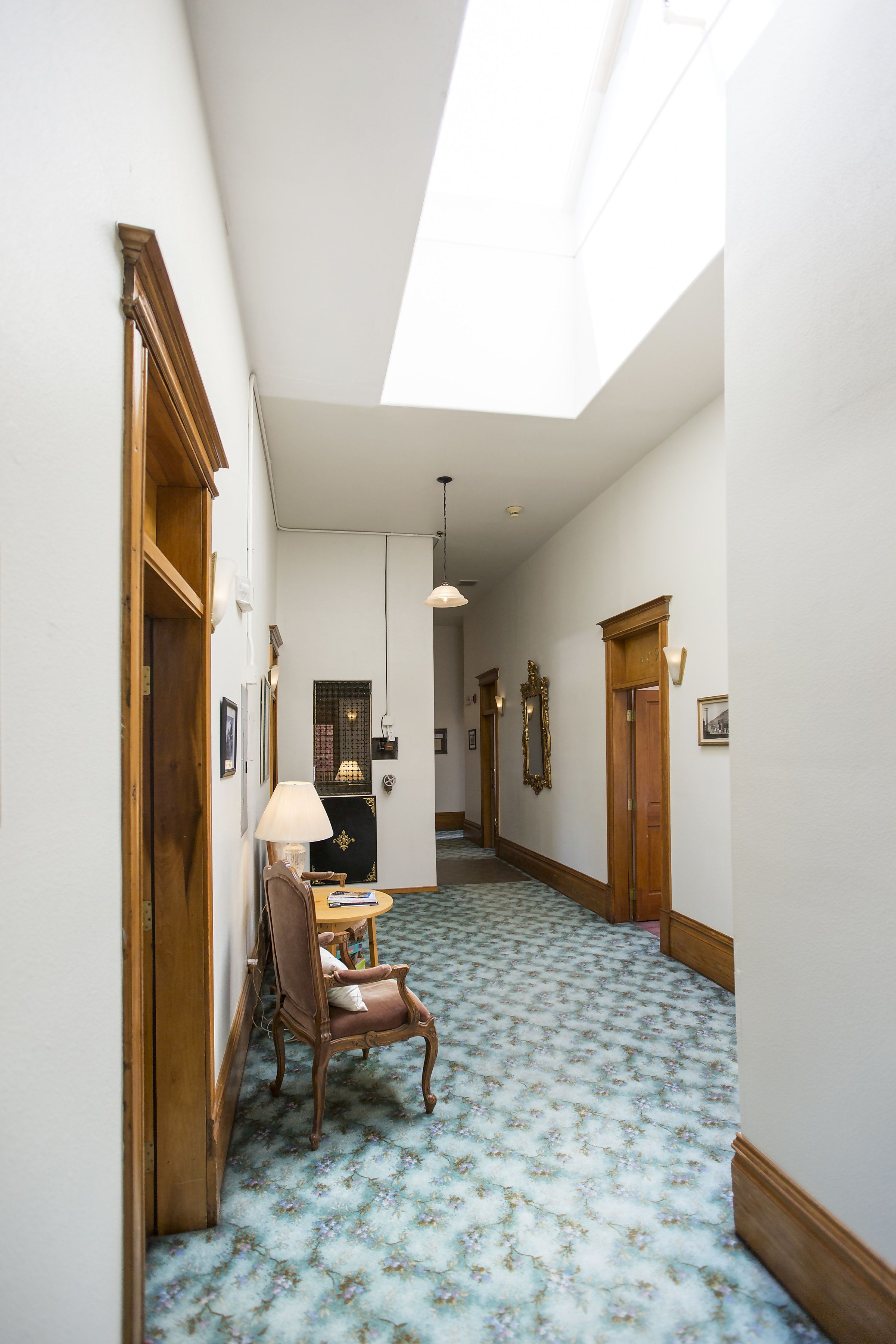 Un couloir avec un tapis à motifs, des portes en bois et une chaise avec une lampe.