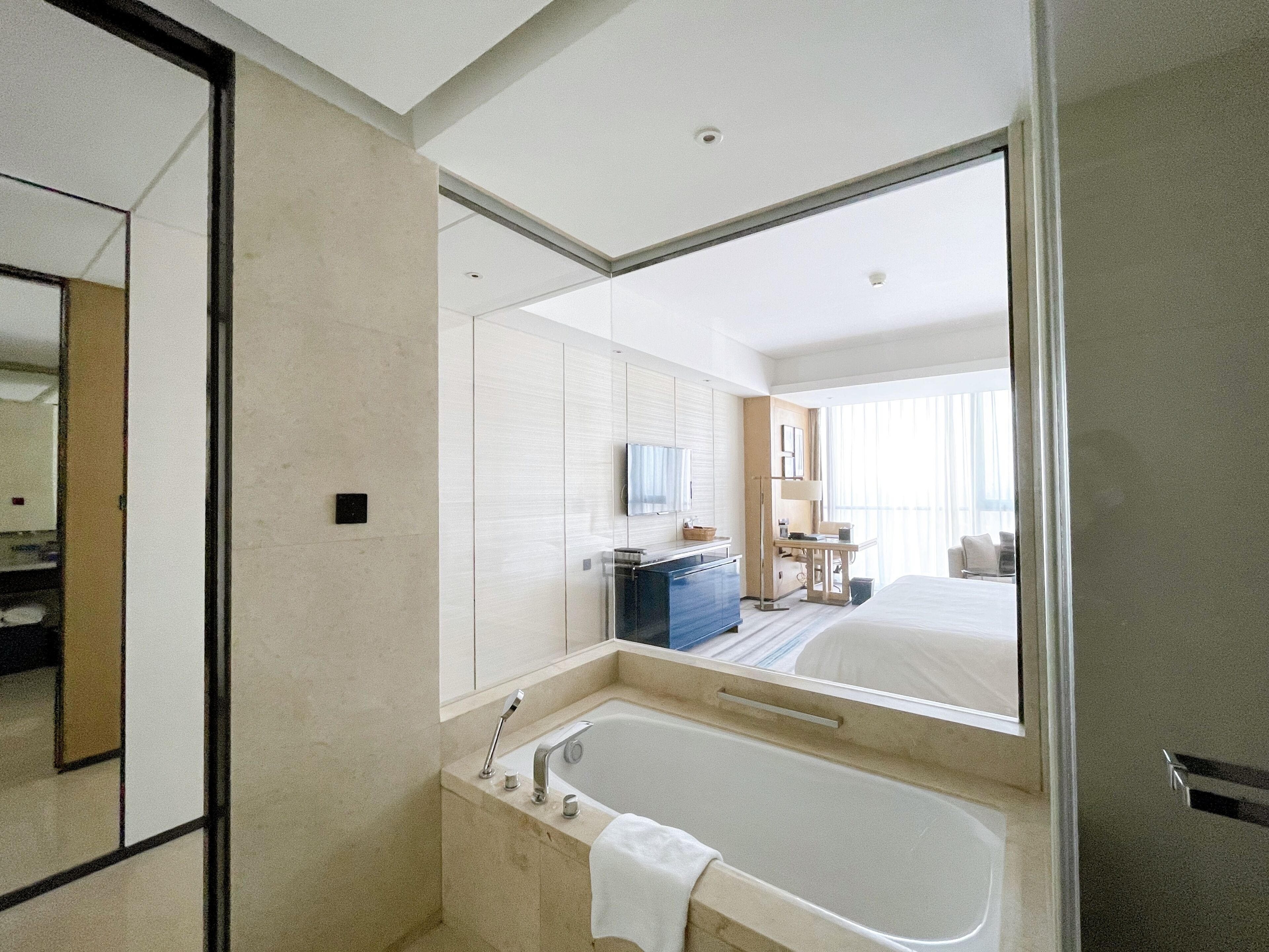 Um banheiro de hotel moderno com uma banheira grande, um espelho e vista para o quarto adjacente.