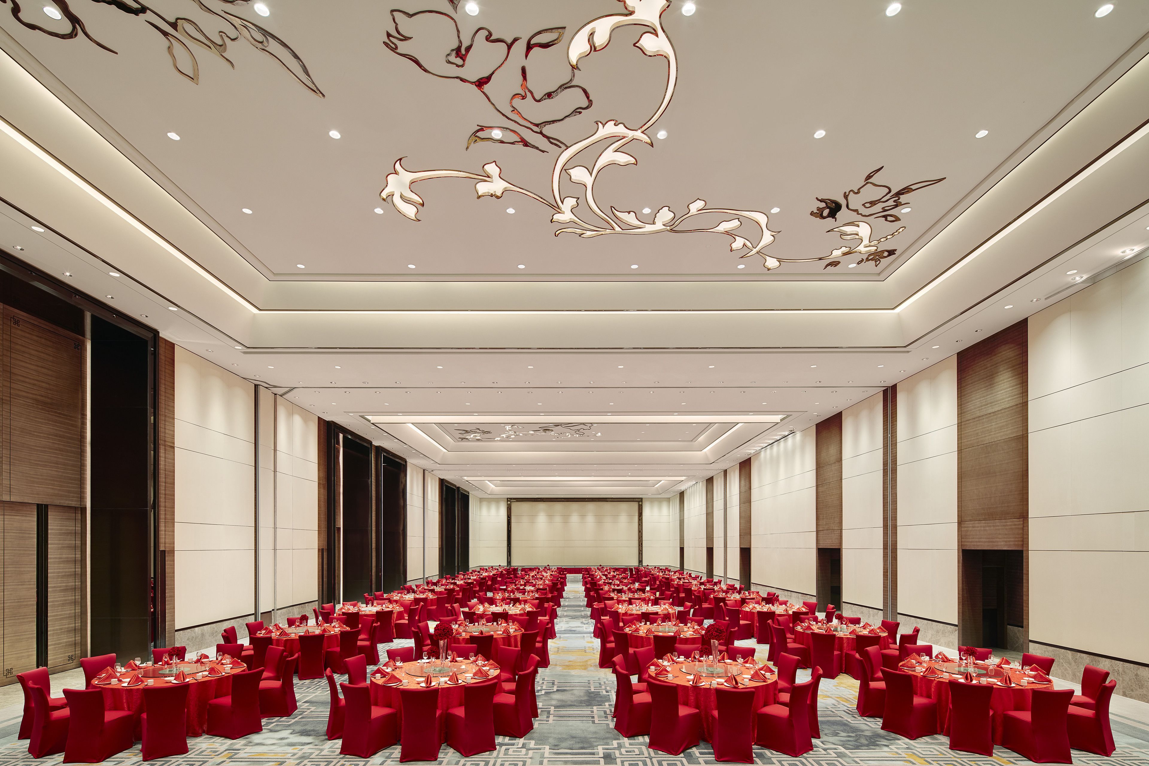 A large conference room with rows of tables and chairs, a decorative ceiling, and a neutral color scheme.