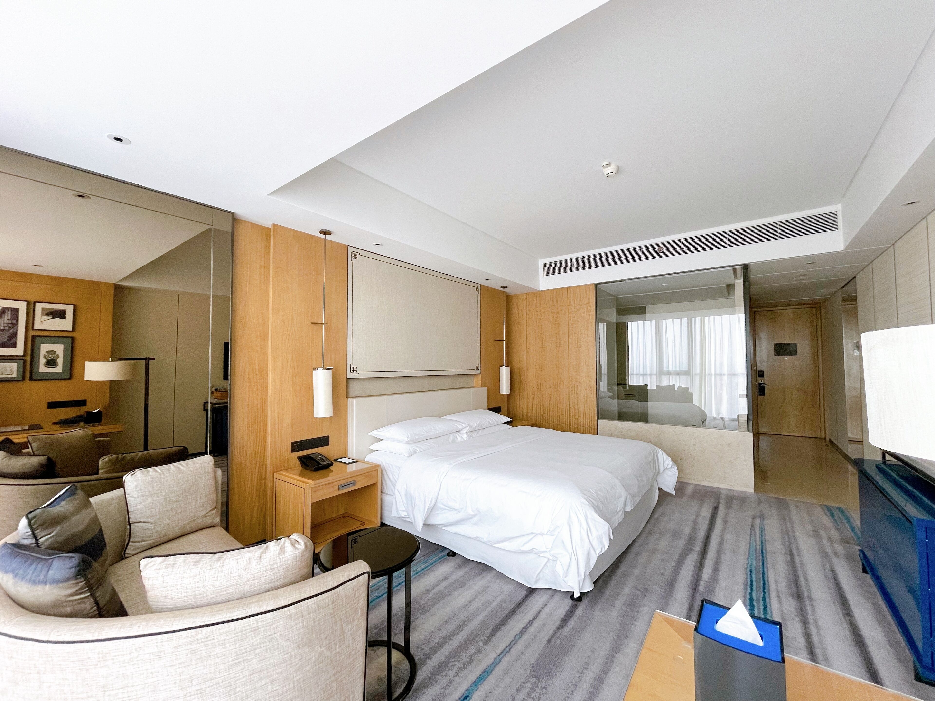 Ein Hotelzimmer mit Bett, Schreibtisch, Stuhl, Nachttisch, Spiegel und Kleiderschrank.
