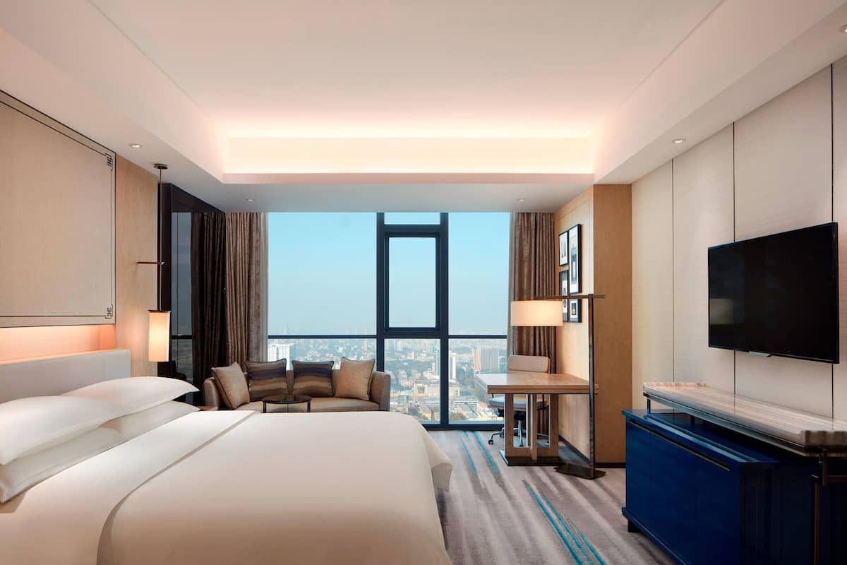 Ein modernes Hotelzimmer mit einem großen Bett, einem Schreibtisch, einem Fernseher und Blick auf die Stadt.
