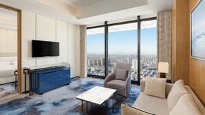 Habitación de hotel moderna con vista a la ciudad, televisor de pantalla plana, sofá, mesa de centro y alfombra azul.