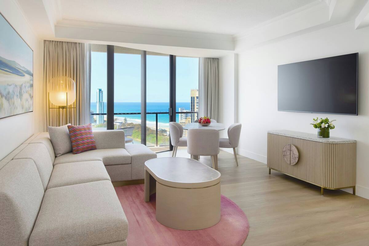Een moderne hotelkamer met een groot raam, een flatscreen televisie, een bank, een salontafel en een dressoir.