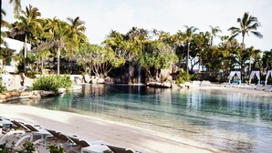 Un área de piscina con sillones de descanso, palmeras y una cascada.