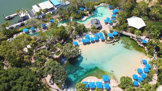 Vista aérea de un resort con piscina central, áreas de descanso alrededor y un muelle.
