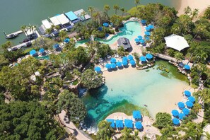 An aerial view of a resort with a central pool, surrounding lounge areas, and a dock.