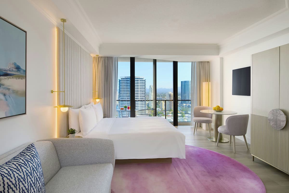 Een hotelkamer met een bed, een slaapbank, een bureau en uitzicht op de stad.