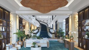 Un hall espacioso con una escalera central, mobiliario moderno y plantas decorativas.