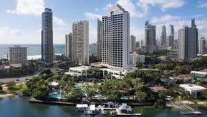 Un hotel de altura con zona de piscina, rodeado de otros edificios y una masa de agua.