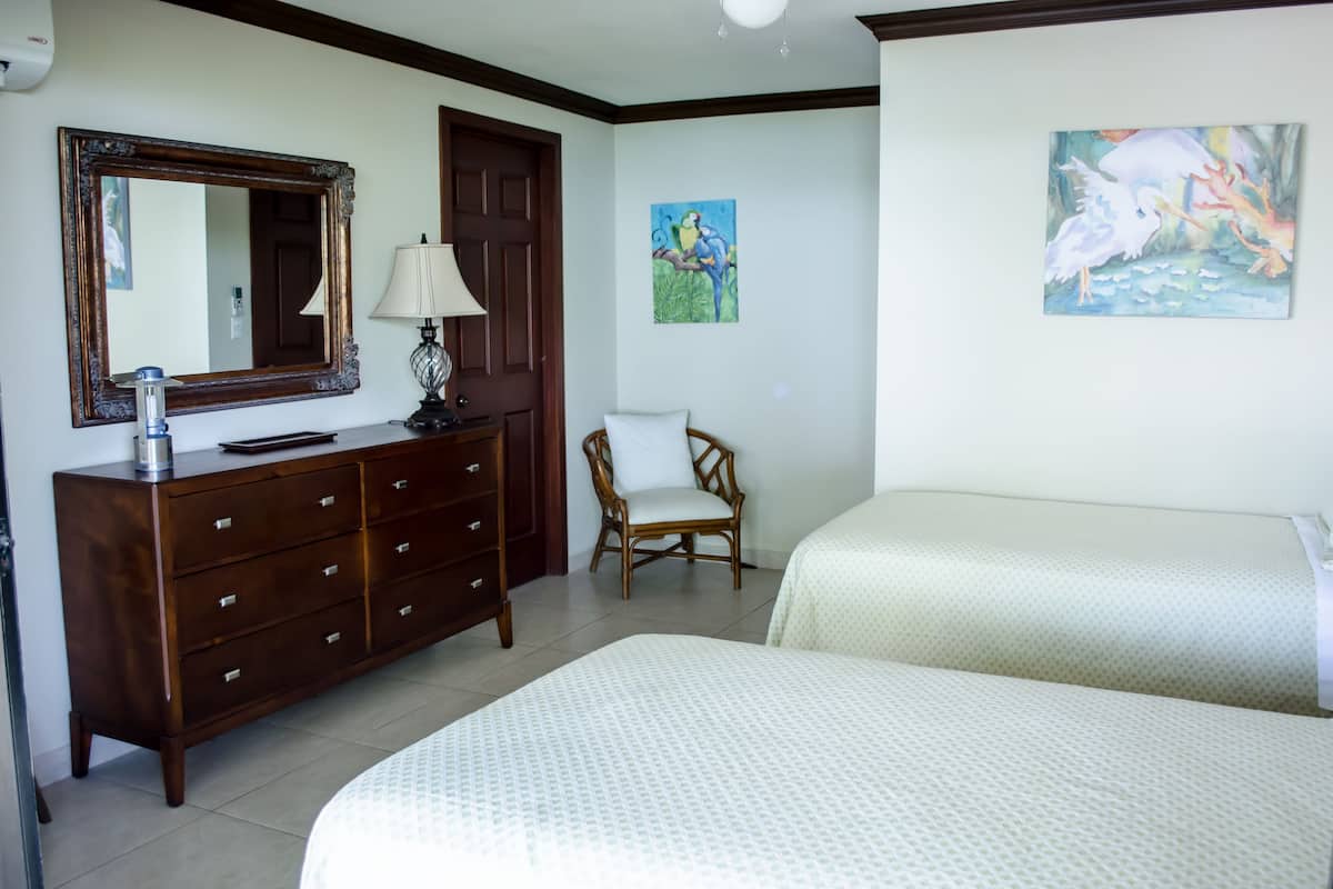 Habitación de hotel con dos camas, un aparador de madera, una silla, un espejo y obras de arte en las paredes.