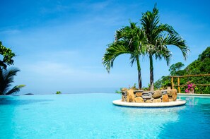 A clear blue pool with a palm tree and a stone structure in the center.