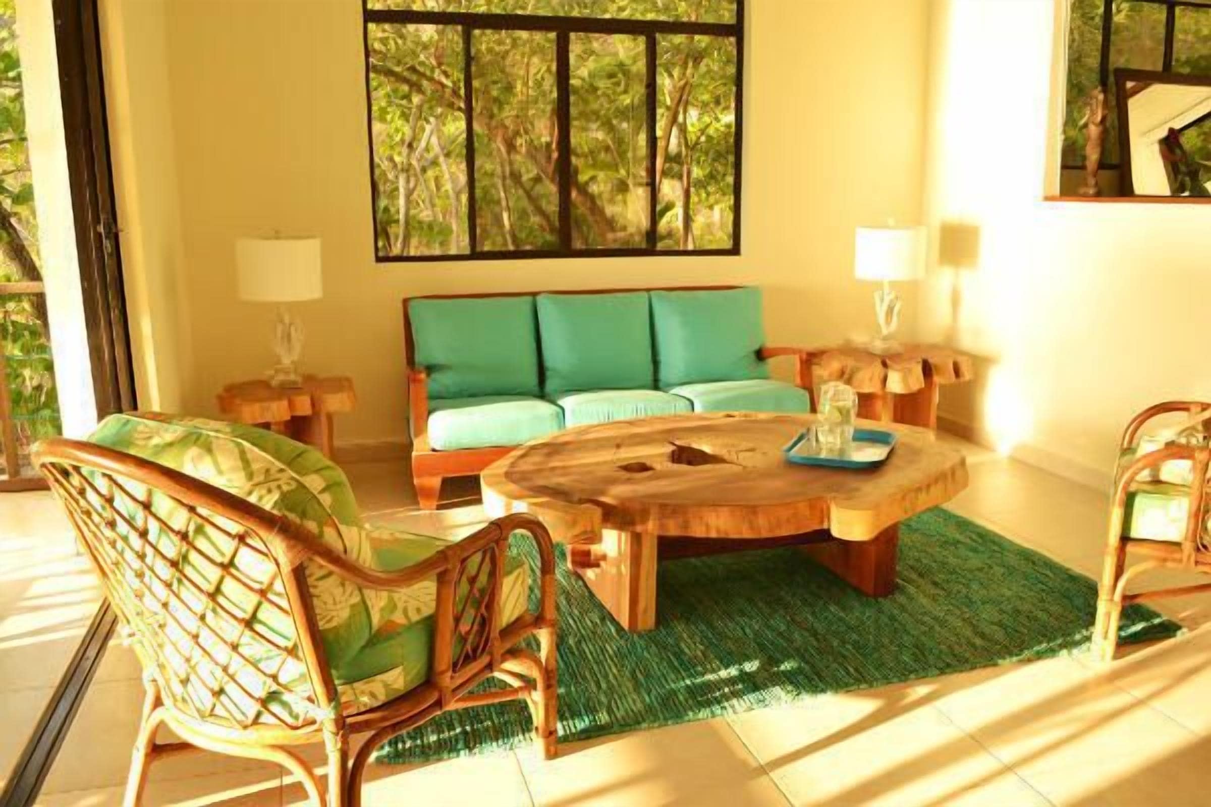 A room with a wooden coffee table, a sofa with green cushions, and wicker chairs.