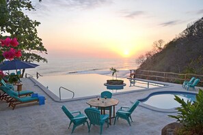 A pool area with lounge chairs and a table, overlooking the ocean at sunset.