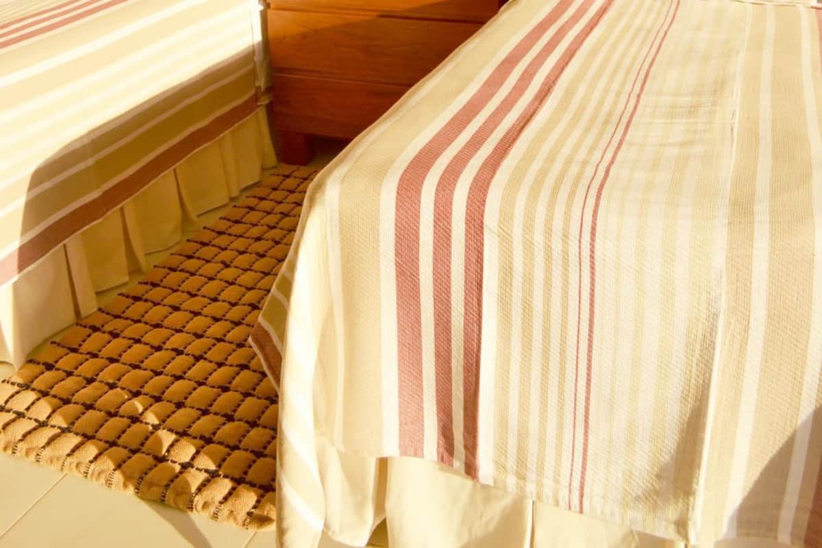 Habitación de hotel con dos camas, una mesita de noche de madera, una lámpara y una alfombra estampada.