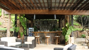 An outdoor bar area with wicker furniture, a stone wall, and a wooden pergola. - Paraiso Escondido Hotel Villas & Resort (Teotepeque)