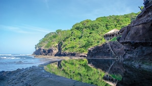 A beach with a clear view of the ocean, a rocky cliff, and a thatched-roof structure. - Paraiso Escondido Hotel Villas & Resort (Teotepeque)
