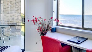 Ein Zimmer mit Meerblick, ein Fenster mit einem Laptop, eine Vase mit roten Blumen und ein roter Sessel.