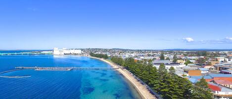 A coastal town with a clear blue sea, a pier, and buildings along the shoreline.